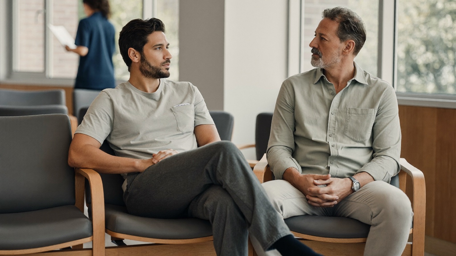 Two men of different generations, one in his twenties and one in his fifties, chatting in a bright clinic waiting area