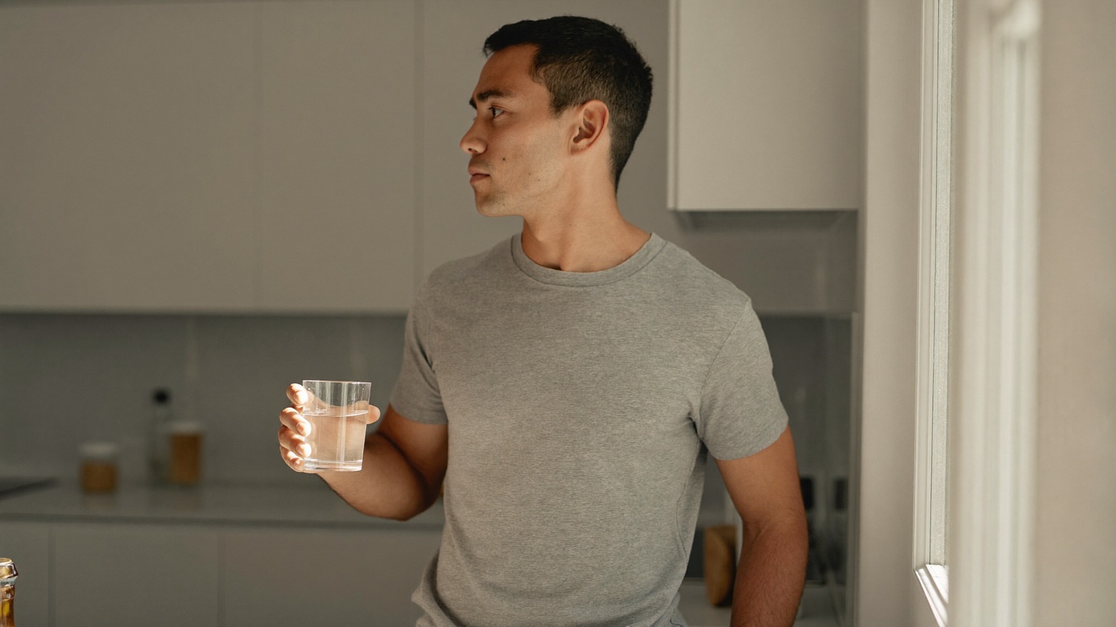 Man holding a glass of water at a kitchen counter in morning light