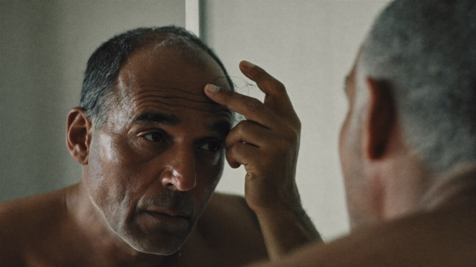 Man examining his receding hairline closely in a bathroom mirror